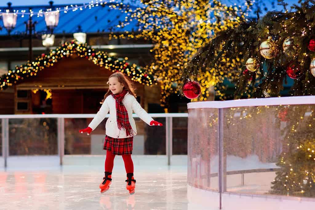 Pattinaggio sul ghiaccio per bambini nella pista di pattinaggio del parco invernale.  Pattinare sul ghiaccio per bambini alla fiera di Natale.  Bambina con i pattini in una giornata fredda.  Divertimento all'aria aperta sulla neve per bambini.  Sport invernali.  Vacanza di Natale in famiglia con bambino.