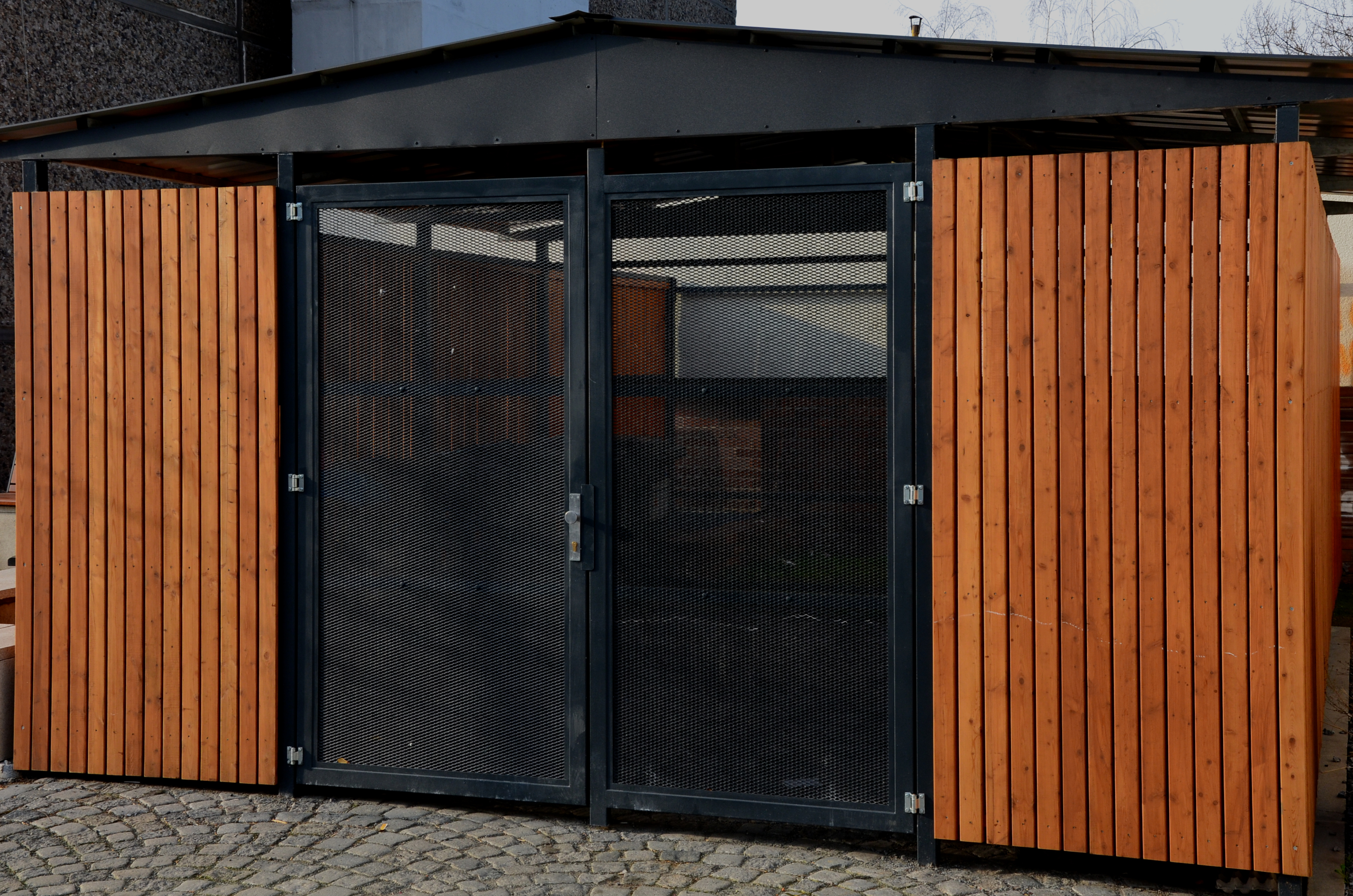 garage con pannellatura in legno e porta in rete trasparente. deposito bidoni vicino alla pensione. protegge la proprietà e l'ordine dei cittadini nel rifugio chiuso. parcheggio auto sicuro e senza neve, ciottolato
