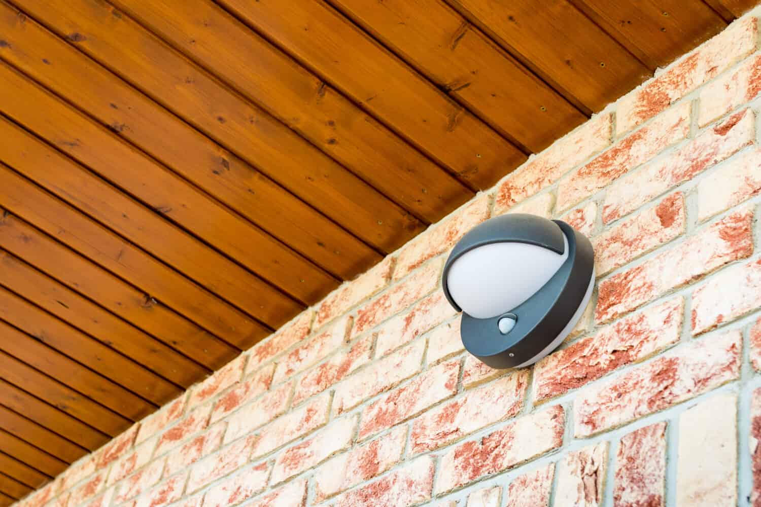 Lampada da parete moderna con sensore di movimento e luce sul muro di mattoni - lampada da parete o da percorso per edifici o case dal design moderno - luce del portico attivata dal movimento - parte del sistema di sicurezza domestica