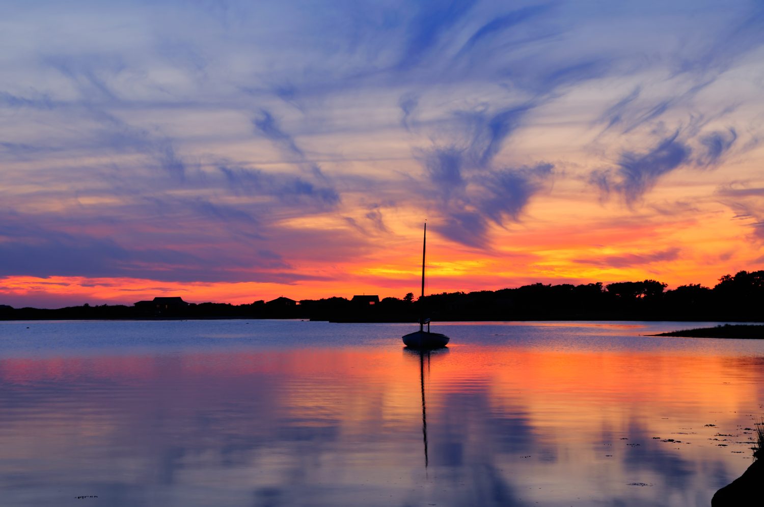 Tramonto e barca a vela a Martha's Vineyard, Massachusetts.  Cielo drammatico con un vivido paesaggio nuvoloso arancione e blu riflesso sull'acqua