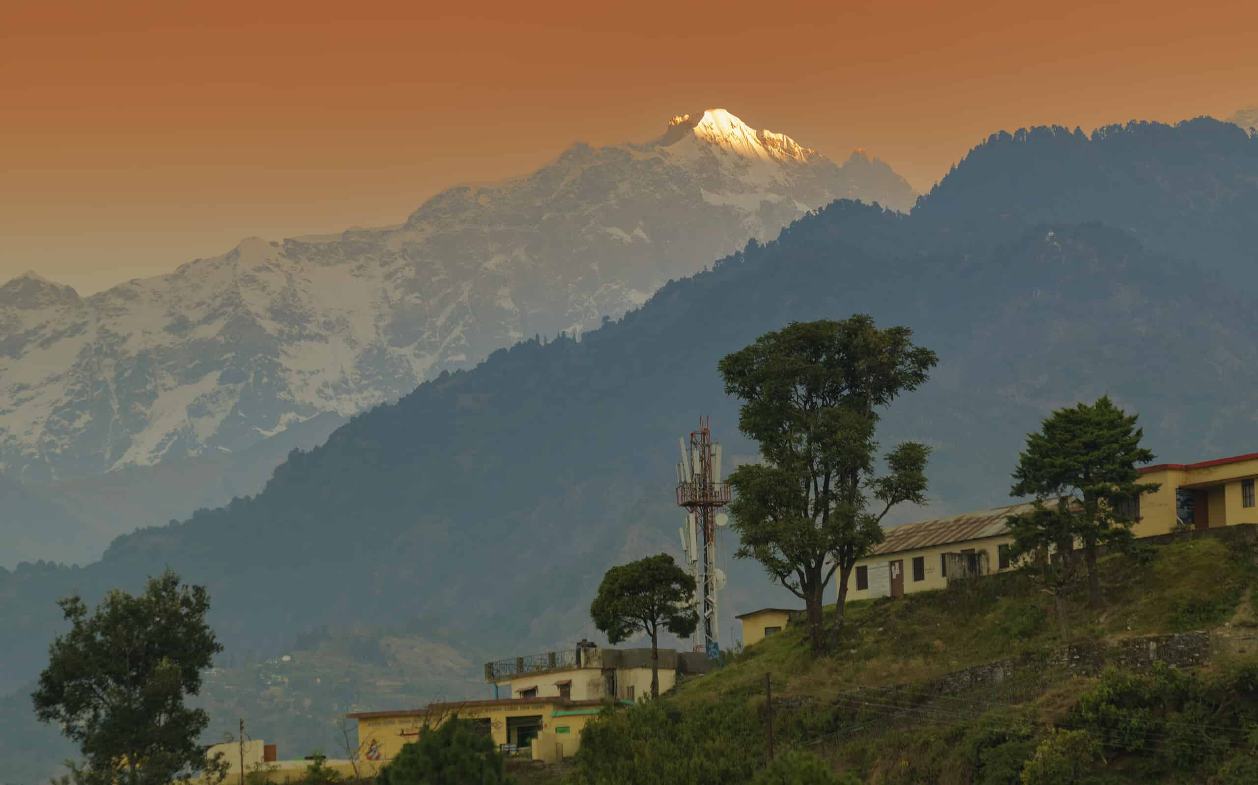 Picco di montagna innevato della gamma Choukhamba con bungalow turistici e resort a Deoriatal, Uttarakhand, India.  Il sole tramonta la luce sulla cima della famosa catena montuosa dell'Himalaya Garhwal.