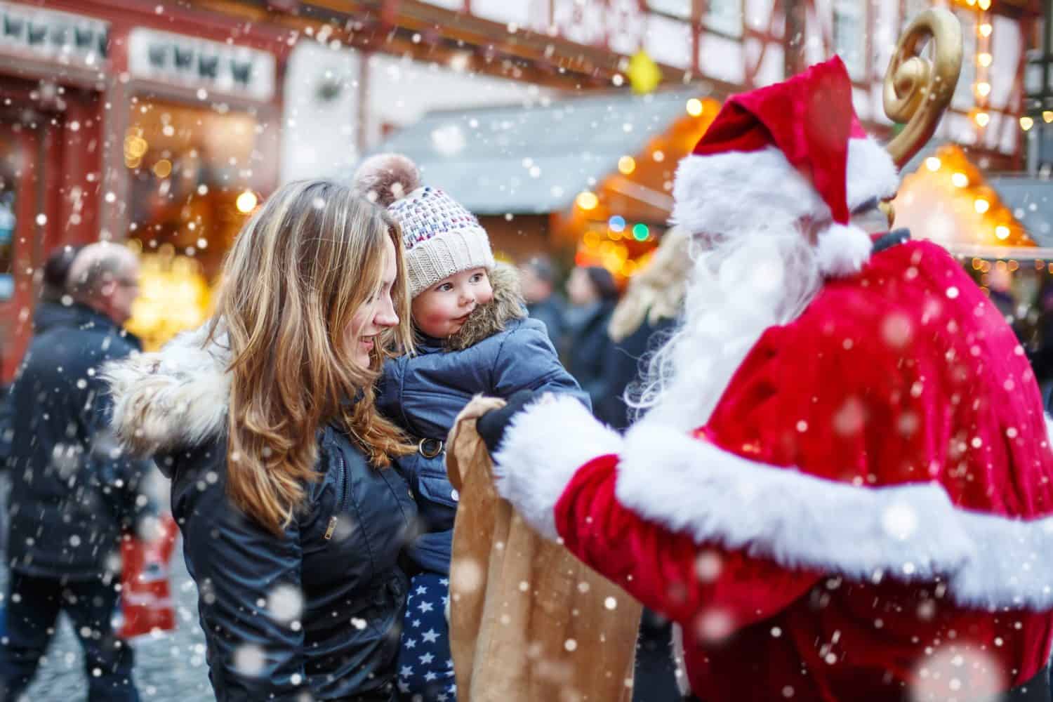 Ragazza carina del bambino con la madre sul mercatino di Natale.  Bambino felice e divertente che prende il regalo dal sacchetto di Babbo Natale.  concetto di vacanze, natale, infanzia e persone.  Famiglia felice durante la nevicata in una giornata invernale.