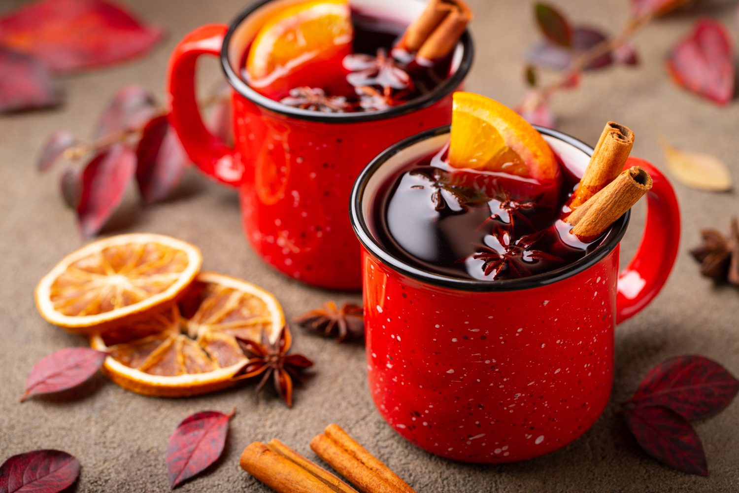 Due tazze di vin brulé autunnale o gluhwein con spezie e fette d'arancia sul tavolo rustico vista. Bevanda tradizionale in vacanza autunnale sullo sfondo delle foglie autunnali