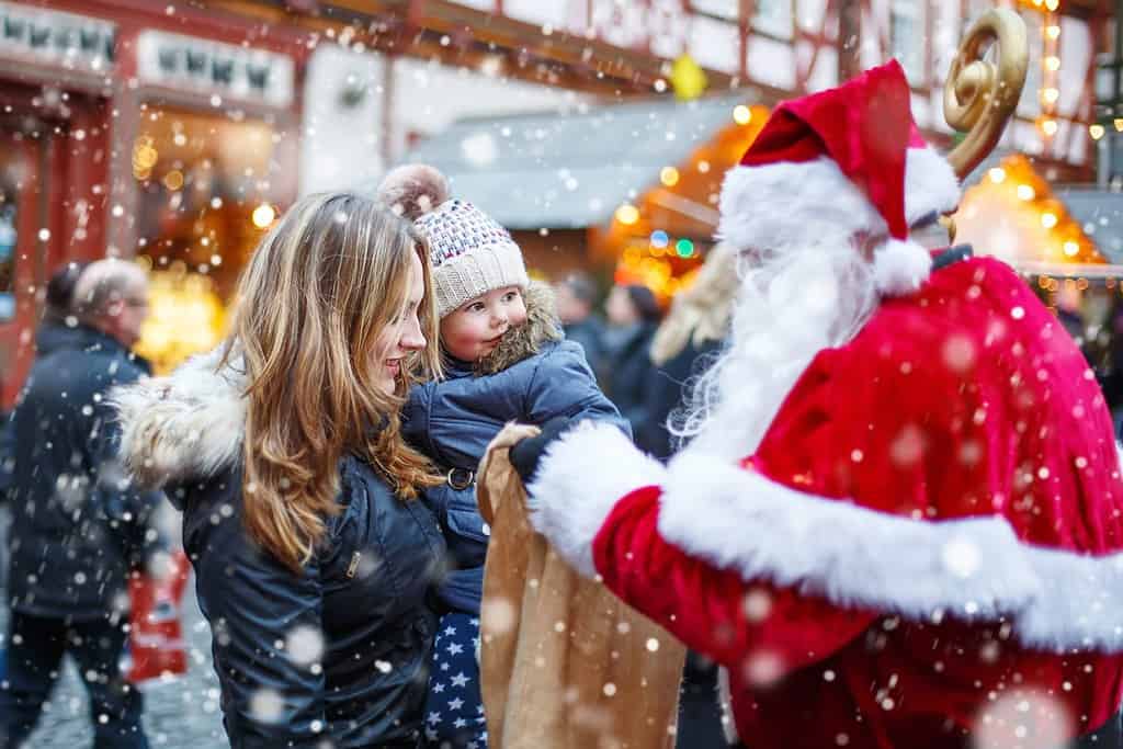 Ragazza carina del bambino con la madre sul mercatino di Natale.  Bambino felice e divertente che prende il regalo dal sacchetto di Babbo Natale.  concetto di vacanze, natale, infanzia e persone.  Famiglia felice durante la nevicata in una giornata invernale.