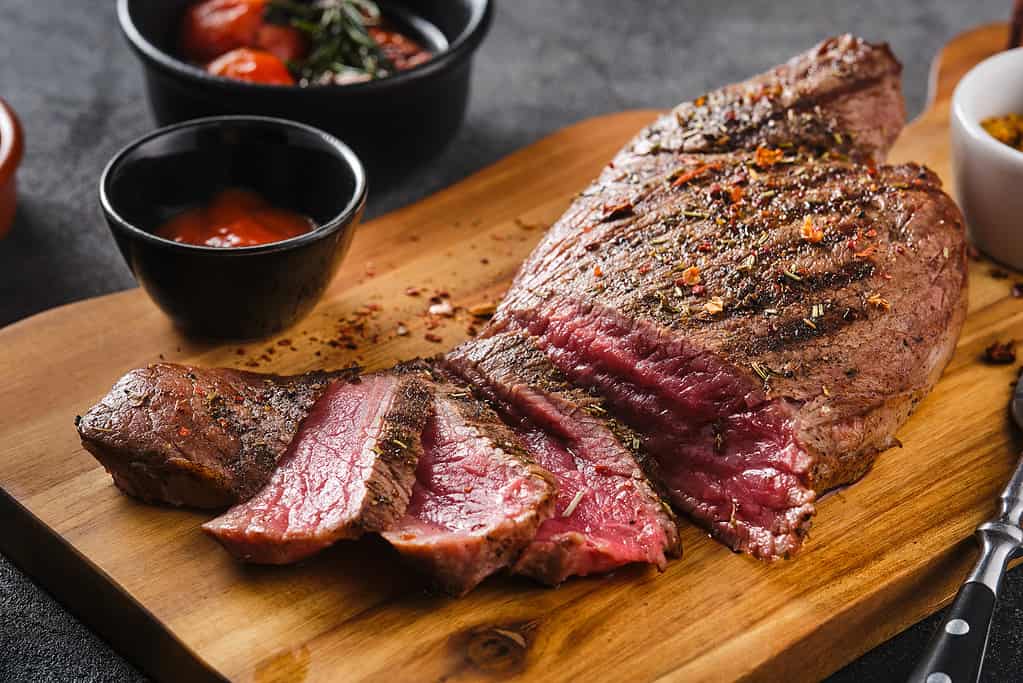 Succosa bistecca di manzo di marmo mediamente cotta con salsa su tavola di legno, primo piano.  Messa a fuoco selettiva.