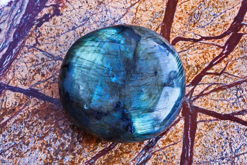 Primo piano del minerale labradorite blu-verde lucidato con pietre preziose naturali su lastra di marmo marrone lucido.