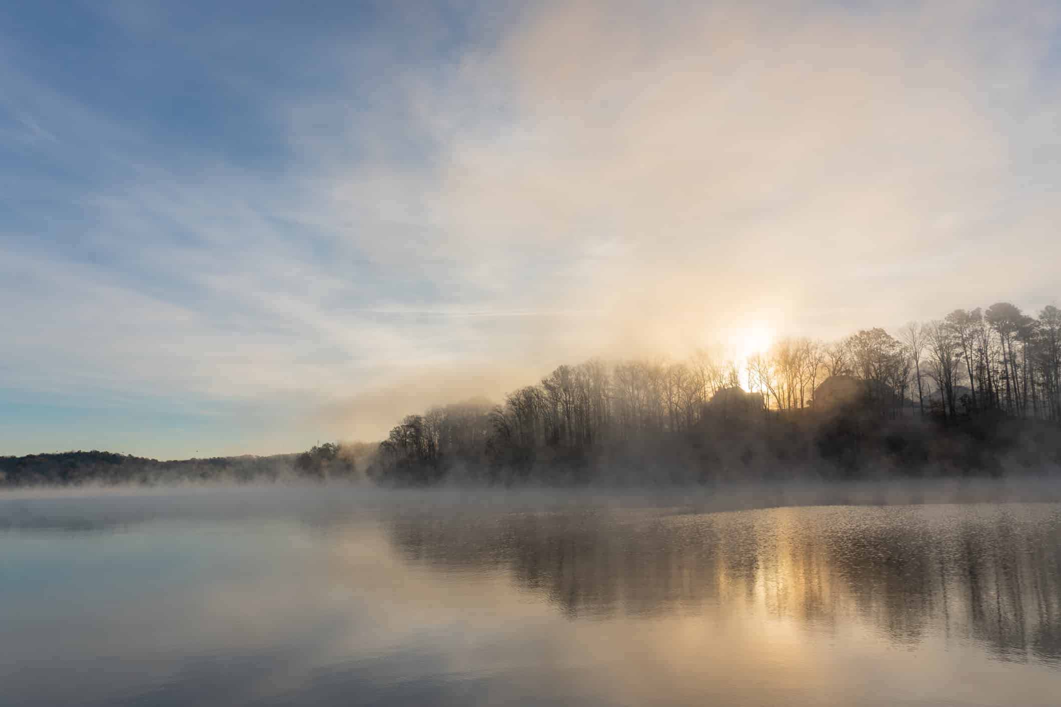 La nebbia sale sulle acque del lago Lanier in Georgia all'alba sotto un cielo blu e arancione;  paesaggio