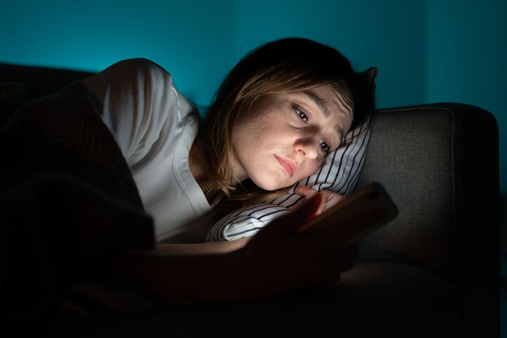 Donna che usa il cellulare mentre giace a letto di notte, soffre di insonnia post-rottura.  Ansia.