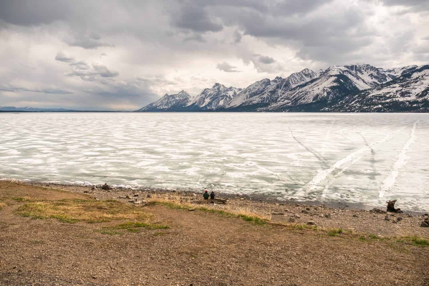 Una coppia seduta su un tronco accanto al lago Jackson ghiacciato nel Parco nazionale Grand Teton, Wyoming
