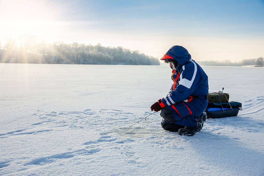 Un pescatore sta pescando con una canna da spinning invernale su un lago ghiacciato. Concerto di pesca sul ghiaccio.