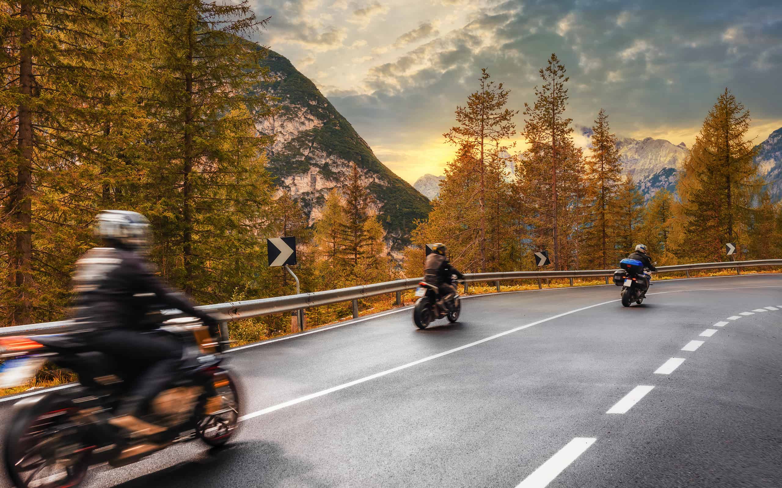 Concetto di viaggio. Gruppo di persone che viaggiano in motocicletta su una strada asfaltata in montagna al tramonto nelle Alpi italiane Bellissimo paesaggio autunnale