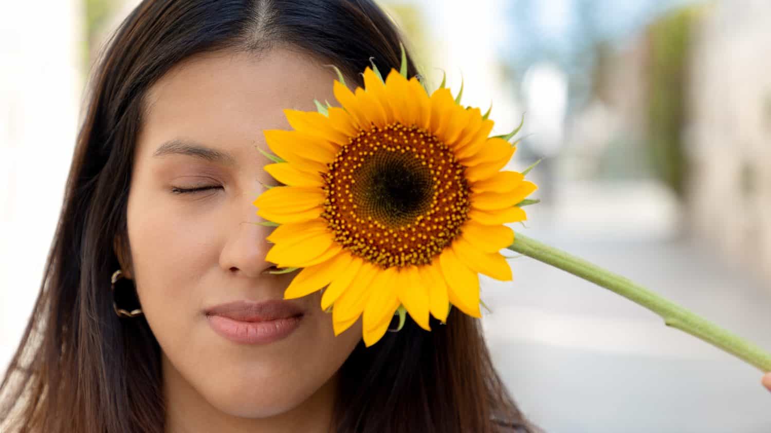 Giovane donna, sorridente e con in mano un girasole in una soleggiata giornata primaverile in un parco, messa a fuoco selettiva, concetto di gioia e fioritura in primavera. Pace, girasoli giganti e gialli.