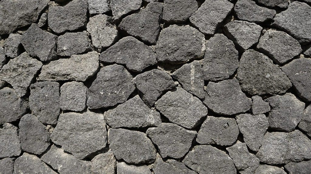 Classico pannello da parete in basalto andesite realizzato con rocce nere impilate. Costruzione di pareti vintage realizzate con pile di pietre naturali.