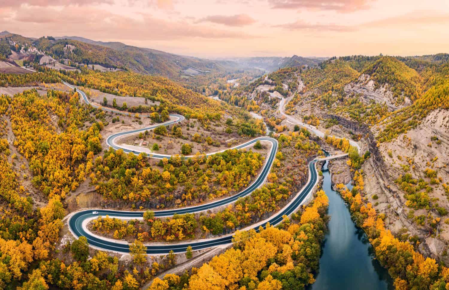 Vista panoramica aerea del fiume Venetikos e della strada tortuosa nella foresta autunnale nella Grecia balcanica.  Parco naturale e infrastrutture di trasporto