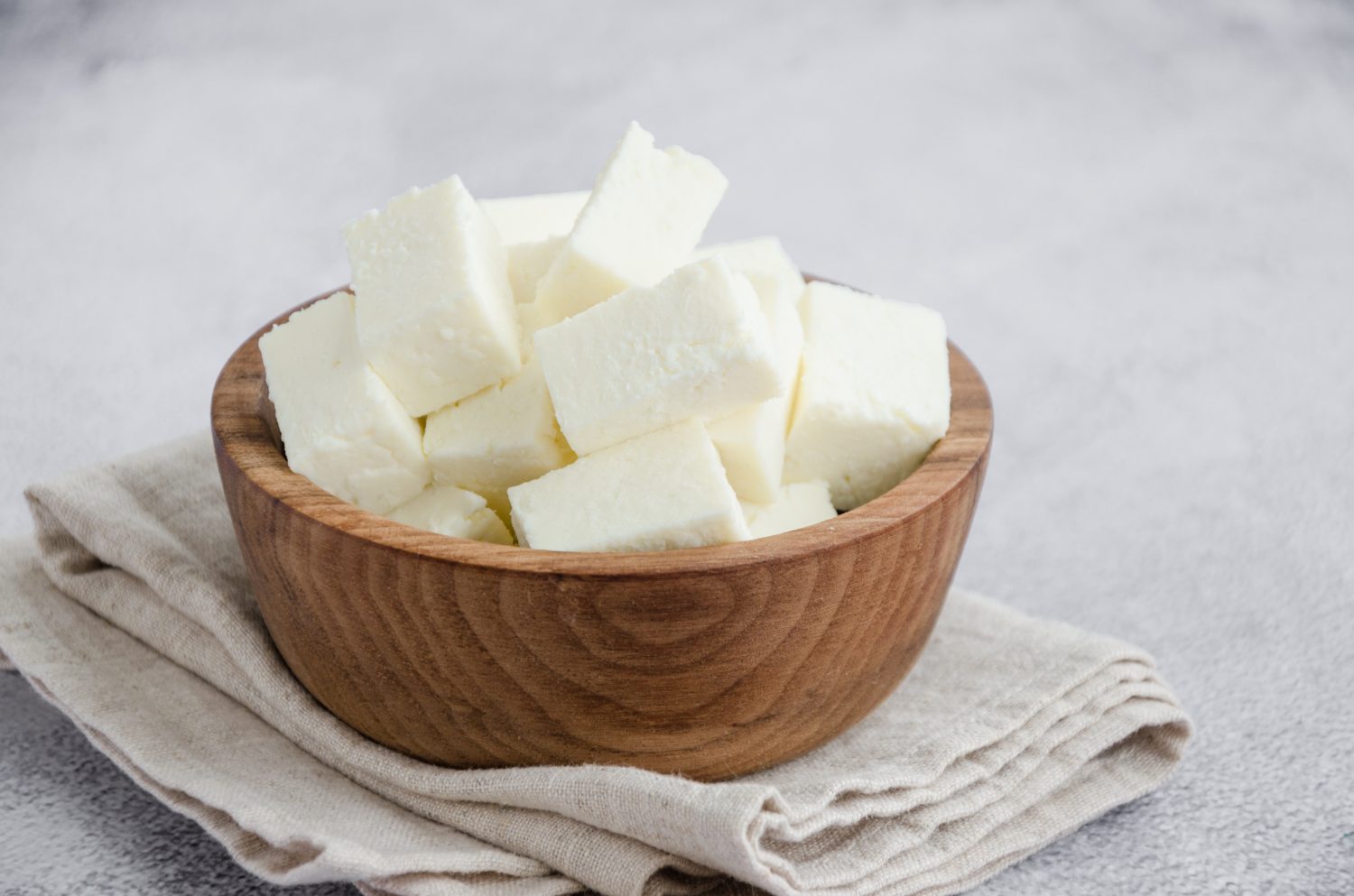 Formaggio paneer indiano fatto in casa a base di latte fresco e succo di limone, tagliato a dadini in una ciotola di legno su uno sfondo di pietra grigia. Orientamento orizzontale. Avvicinamento