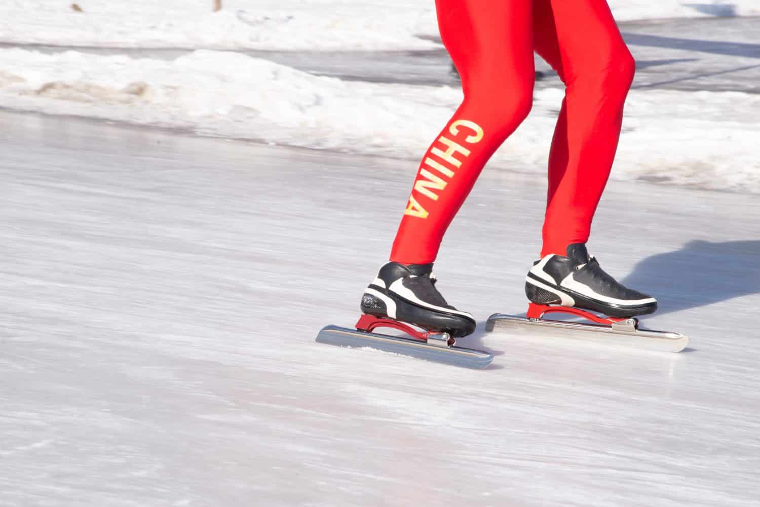 Un giovane uomo attivo si diverte a pattinare sul lago ghiacciato con collant cinesi nel parco di Shenyang.  Primo piano dei collant rossi, degli stivali, delle lame e delle gambe.