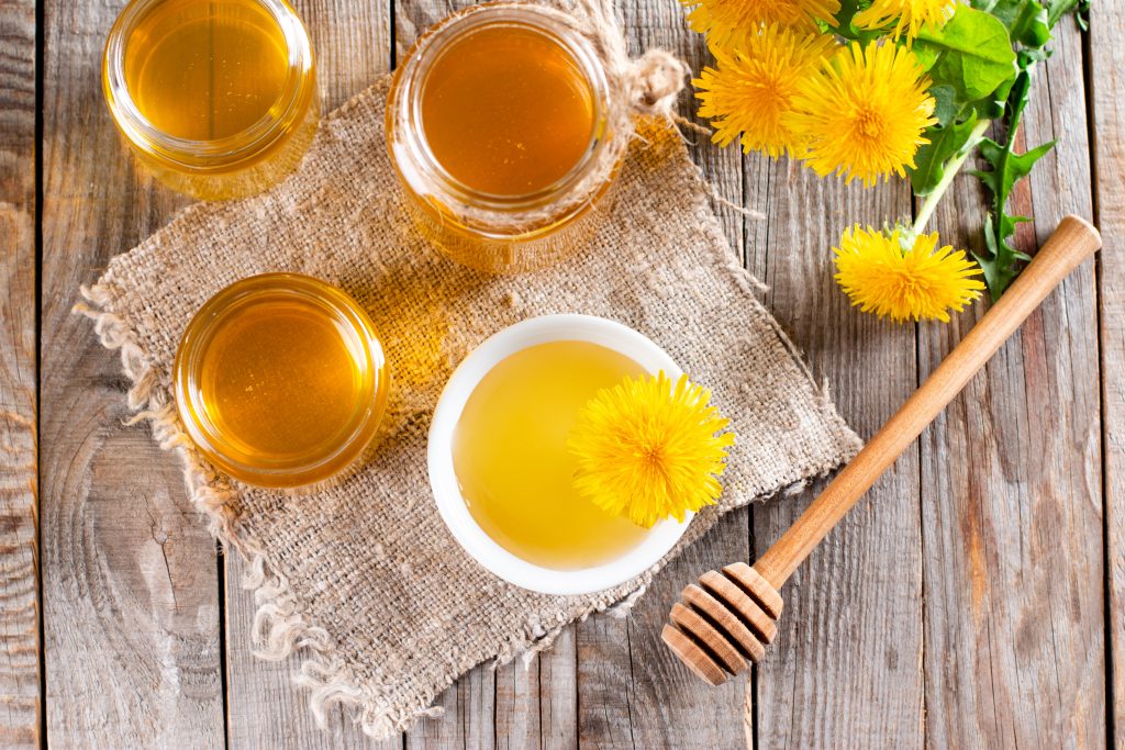 Barattolo di miele, fiore di tarassaco su un tavolo. Concetto di prodotto naturale, rurale, biologico e sano. Vista dall'alto. Copia spazio