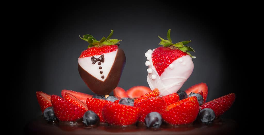 Sposo della sposa della coppia nuziale della fragola alla torta nuziale al cioccolato. Dolciumi di lusso, arte, tendenza, matrimonio, fragole, abbellimento degli sposi, mirtilli e crema glassata. Simbolo alimentare dell'amore