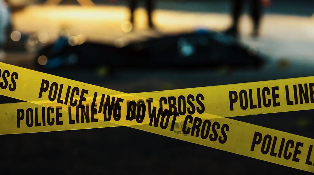 Inquadratura incentrata sul nastro giallo che mostra il testo "La linea di polizia non attraversa".  Nastro utilizzato per delimitare una scena del crimine in cui la scientifica, gli investigatori e i poliziotti stanno lavorando per risolvere un caso di omicidio