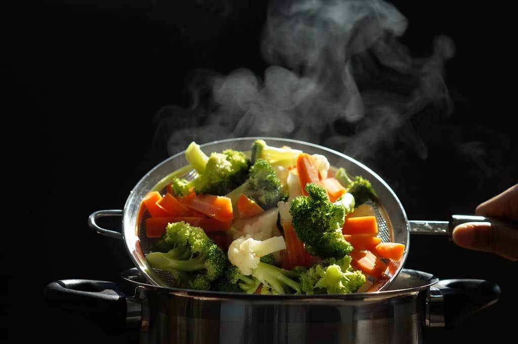 cottura a vapore di verdure bollite calde. Cesto di verdure appena bollite dall'acqua calda con messa a fuoco selettiva del vapore, messa a fuoco morbida. cibo caldo, dieta e concetto sano.