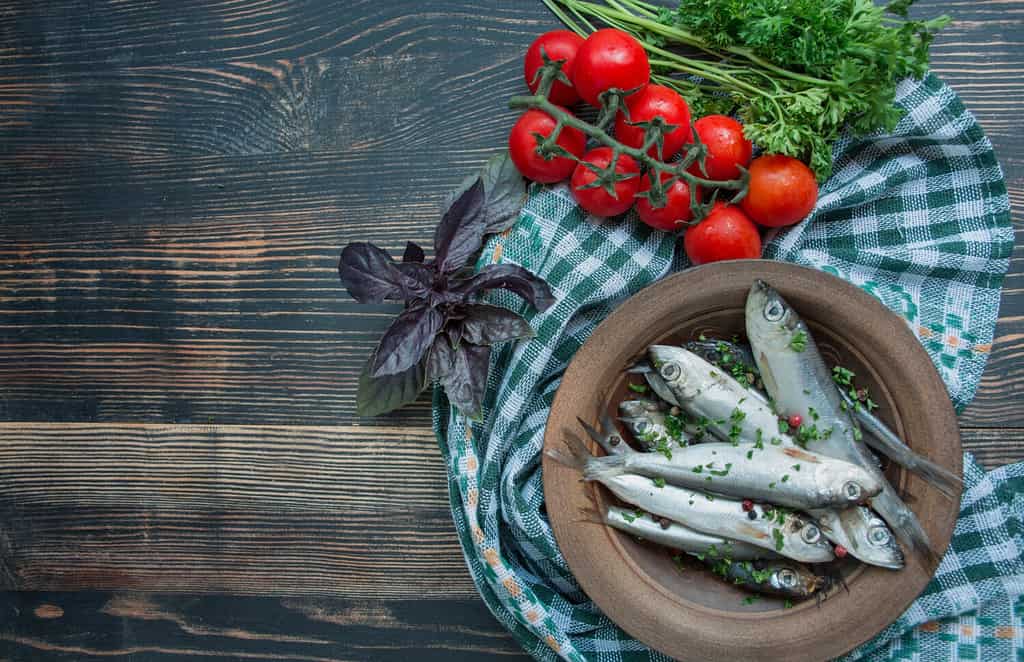 Frutti di mare dell'aringa del Baltico. Pesce aringa salato in una ciotola con spezie ed erbe aromatiche. Sfondo di legno.