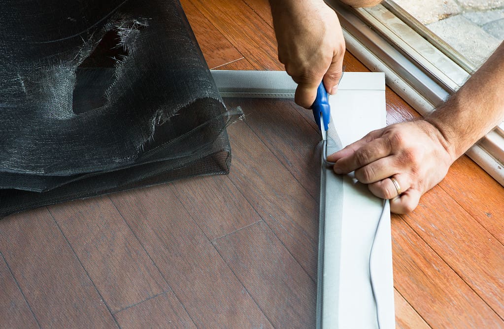 Uomo che sostituisce il vecchio schermo strappato della porta del patio
