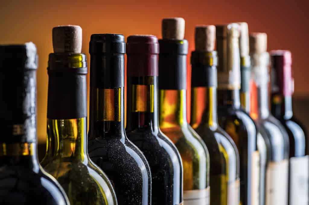 Bottiglie di vino tappate e stappate in primo piano in linea.  Sfondo di vino.