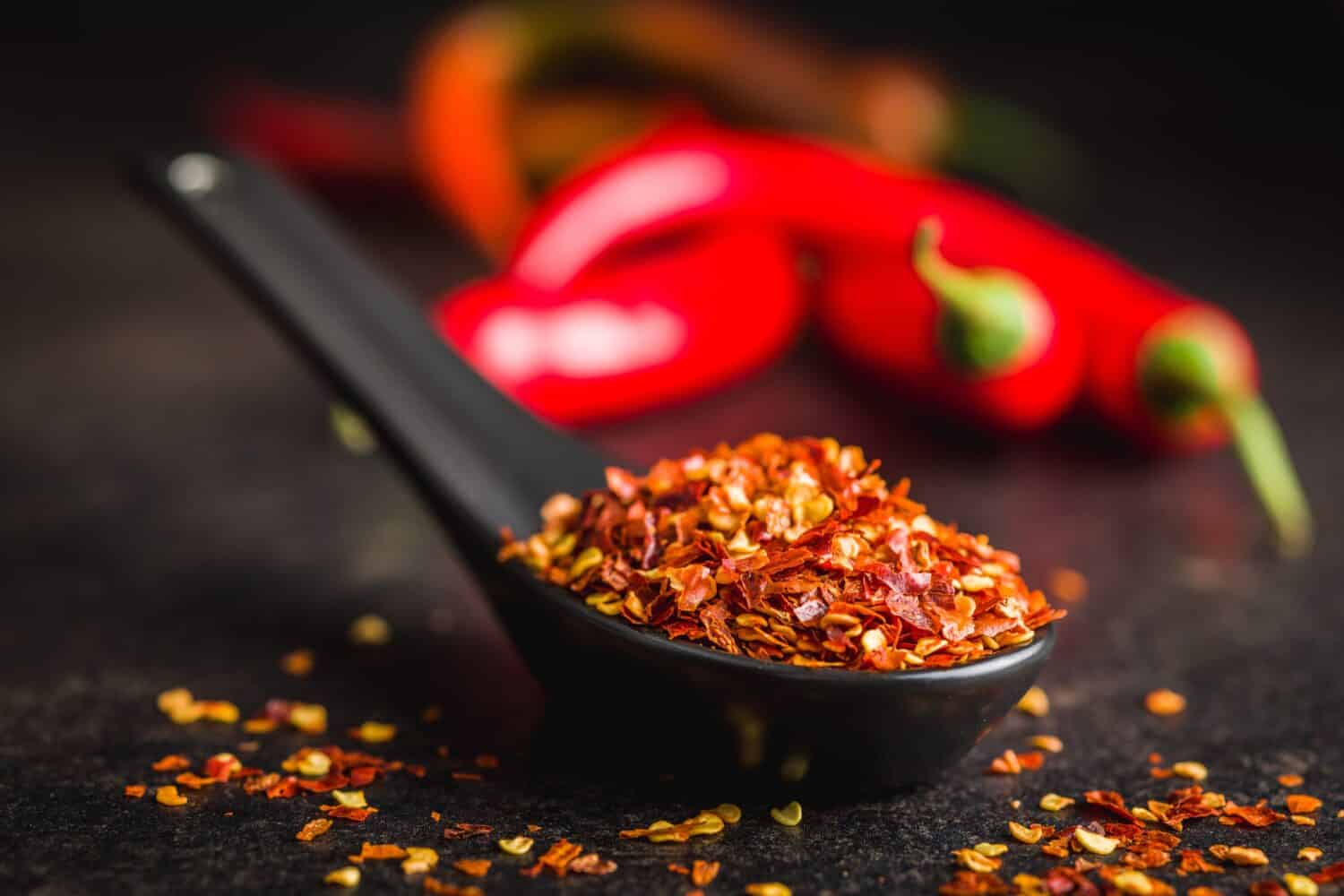 Fiocchi di peperoncino secco.  Peperoni rossi schiacciati in un cucchiaio sul tavolo nero.