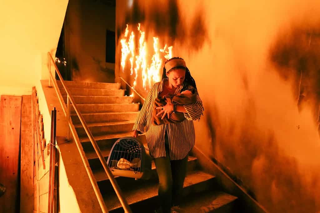 Coraggioso pompiere scende le scale di un edificio in fiamme e tiene tra le braccia la ragazza salvata. Apre il fuoco e un pompiere sullo sfondo.